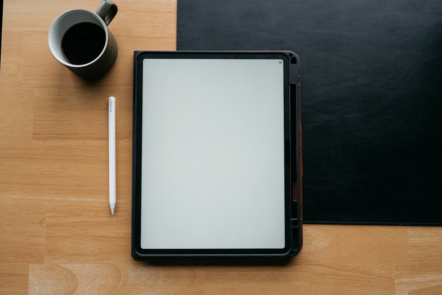 A tablet, stylus, and coffee mug on a wooden desk.