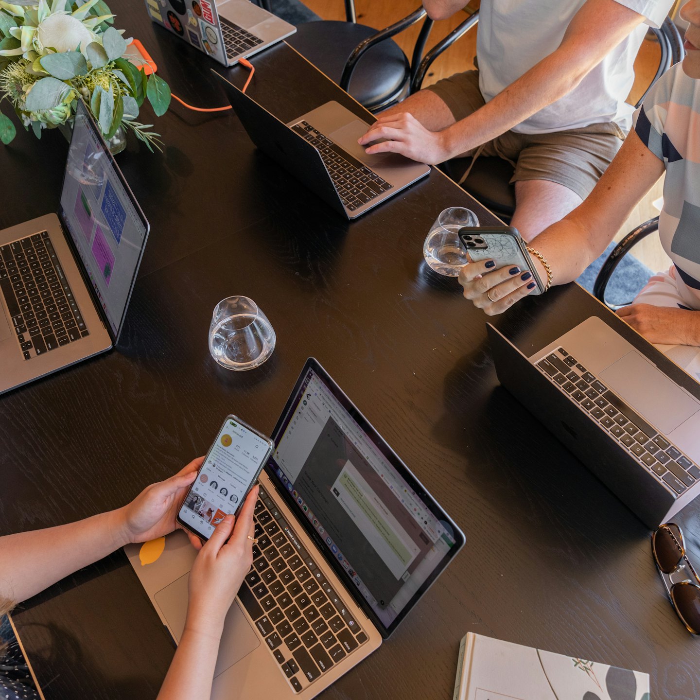 Three people working on laptops at a wooden table.
