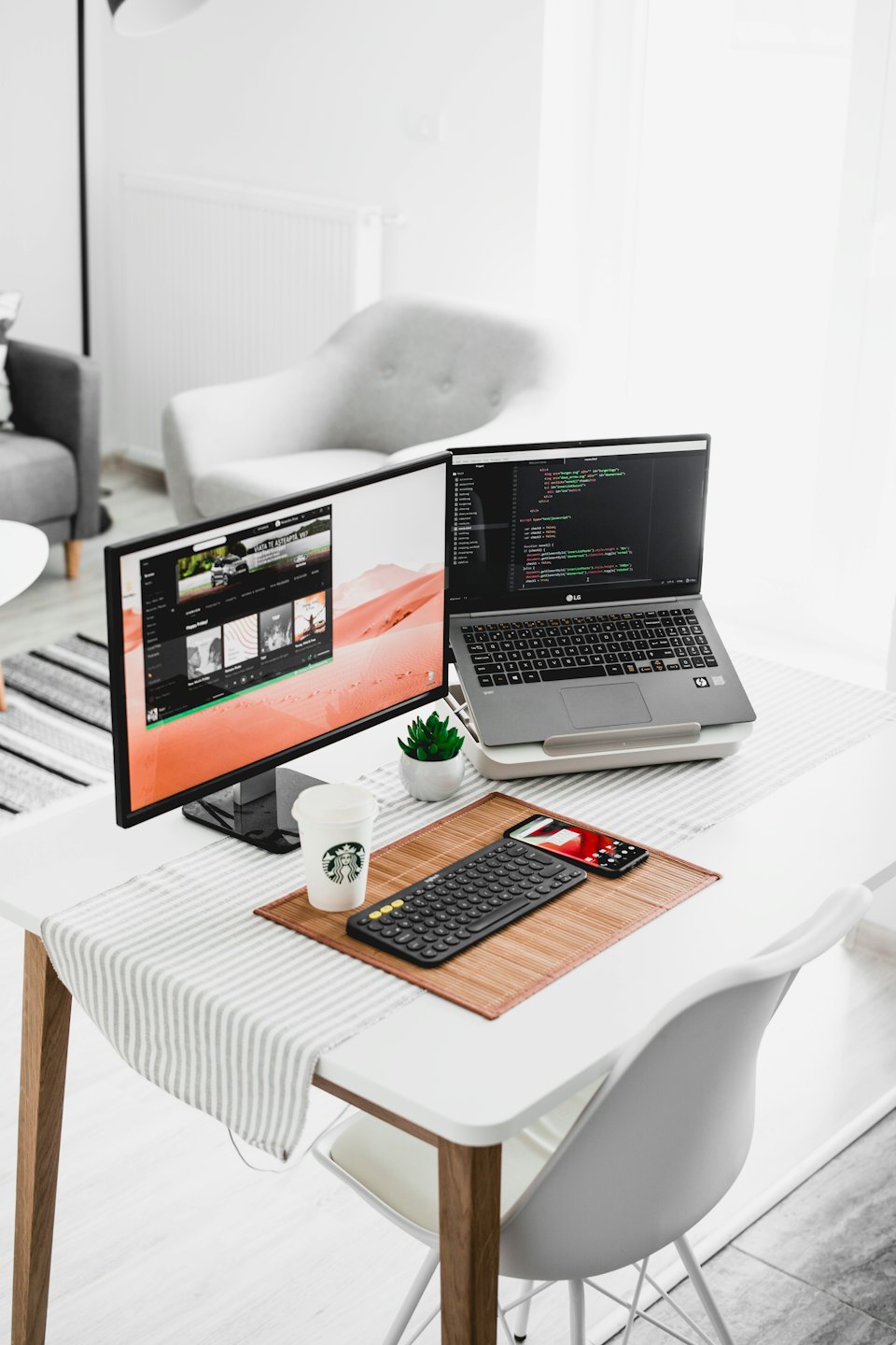 Modern home office with laptop, external monitor showing code, and desk accessories.